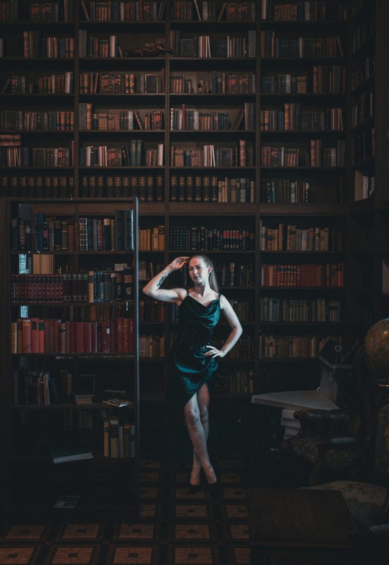Fotografie einer Frau, stehend in einer Bibliothek, grünes, edles Kleid Bücherregale bis an die Decke